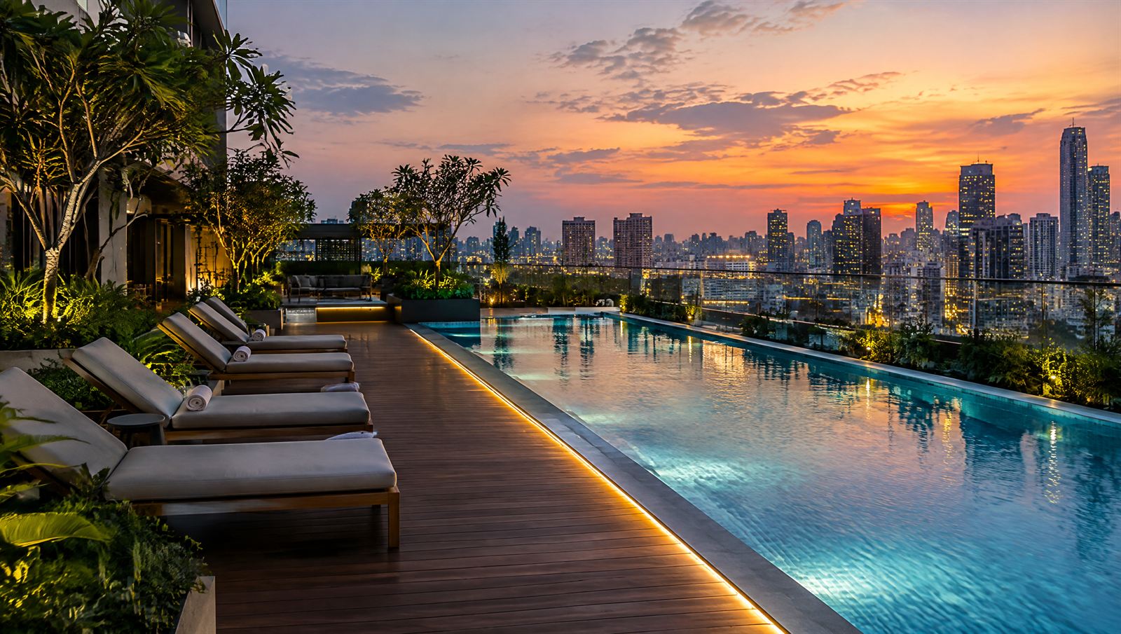 Rooftop lap pool and timber deck at dusk with city lights beyond